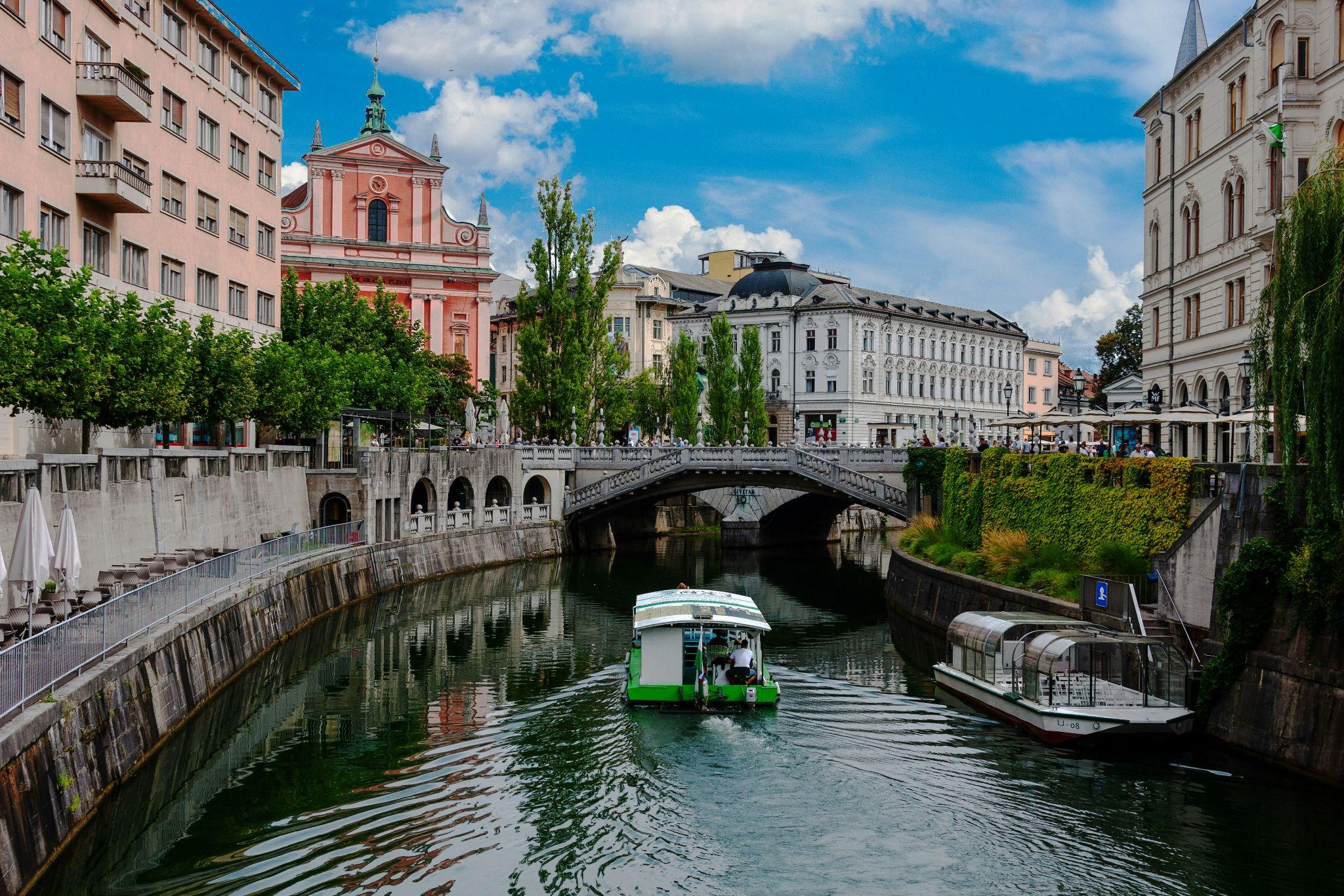 Boats on the Ljubljanica River surrounded by bridges and colorful buildings in Ljubljana.