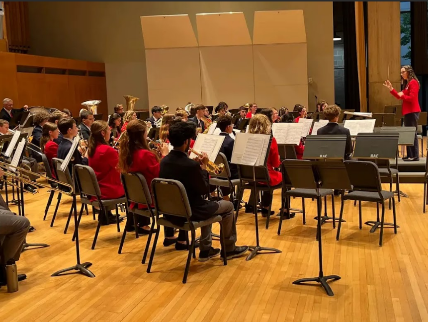 Student musicians seated in a rehearsal hall with music sheets, playing instruments under the guidance of an instructor.