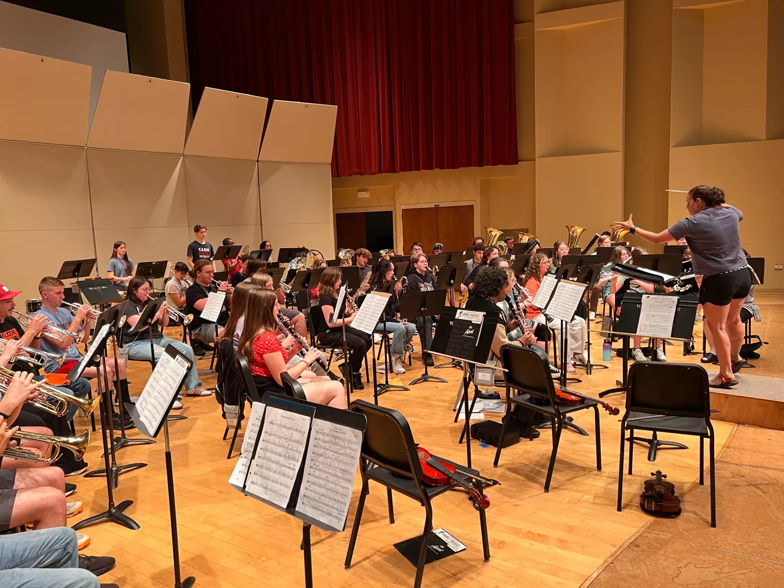 Student orchestra rehearsing in a concert hall with a conductor leading the ensemble.